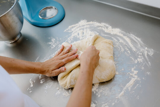 Anonymous woman kneading dough on a stainless steel kitchen surface.