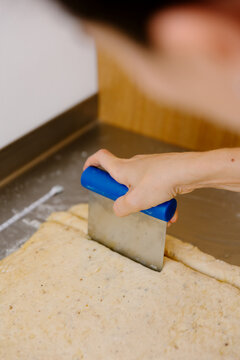 Hand using a pastry spatula to crumble fresh dough on a counter.