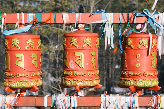 Arshan, Russia - March 29, 2025: Row of traditional red Buddhist prayer wheels with golden Tibetan mantras and colorful ribbons at datsan in Arshan village,&nbsp;Buryatia, Russia on bright winter day