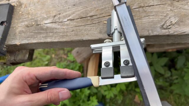 Sharpening kitchen knife with manual knife sharpener system on wooden bench.