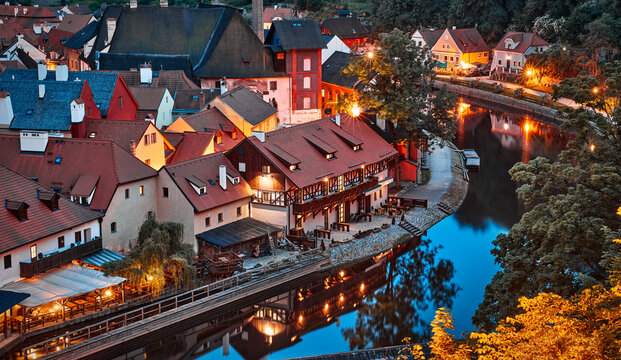 Czech Krumlov Czech Republic. Evening panorama old town illuminated street lamp over river Vltava. Picturesque landscape with authentic houses with red tegular roofs.