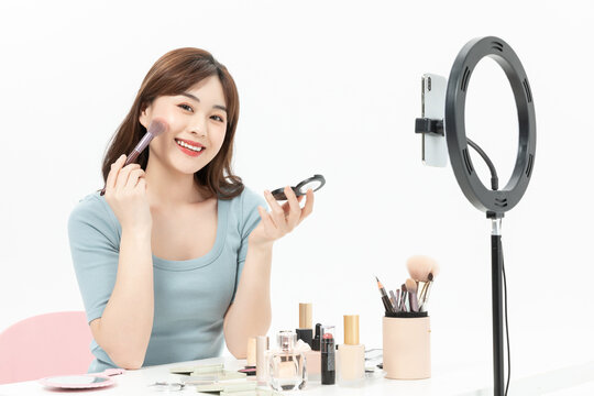 Smiling Asian woman applying makeup while live streaming with a ring light