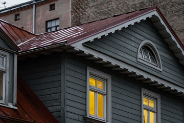 Timber facade with an arched gable window, decorative eaves and illuminated windows beneath a metal roof, showing traditional wooden building envelope and joinery details © K