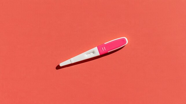 A single pink and white pregnancy test kit resting on a vibrant solid coral orange background