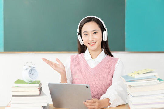 Smiling Young Woman with Headphones Learning Online at Desk with Tablet and Books