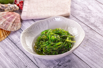 Japanese salad wakame seaweed with sesame seeds in white ceramic bowl on grey wooden table sea shell garnish seaweed appetizer © Andrei Starostin