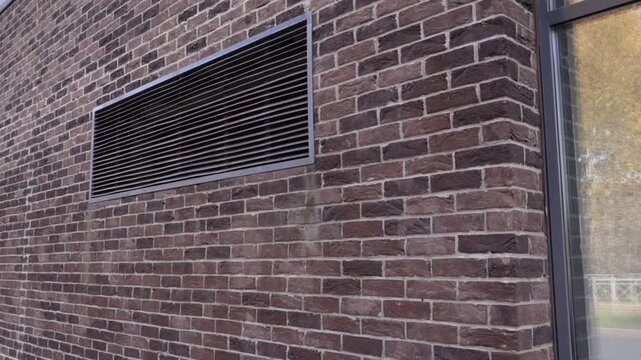 Close-up of dark brown brick wall featuring rectangular ventilation grille and window edge