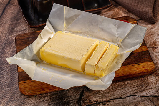 Yellow butter block with slices on parchment paper and wooden board dairy product