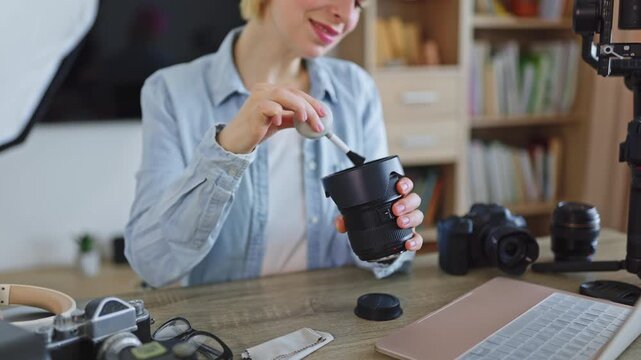 A caucasian woman meticulously cleans her professional camera lens with a blower brush, surrounded by photography equipment