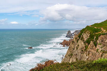 Fototapeta premium Cabo da Roca dramatic coastal cliff overlooking Atlantic Ocean in Portugal. Scenic westernmost point of Europe with rugged landscape, ocean waves and natural coastline.