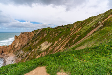 Fototapeta premium Cabo da Roca dramatic coastal cliff overlooking Atlantic Ocean in Portugal. Scenic westernmost point of Europe with rugged landscape, ocean waves and natural coastline.