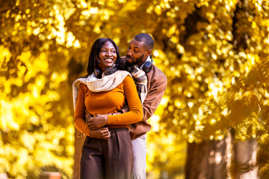African American man leaning on his smiling partner in autumn park