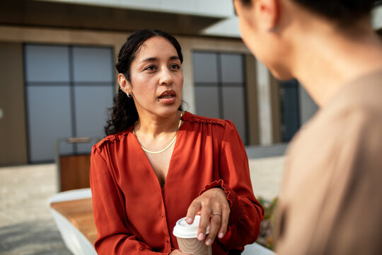 Woman talking with another woman outdoors while holding coffee
