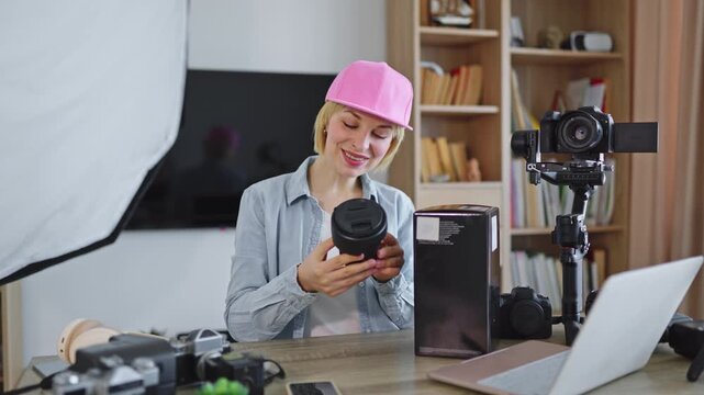 A young woman with a pink cap excitedly unboxes a new camera lens for her content creation setup