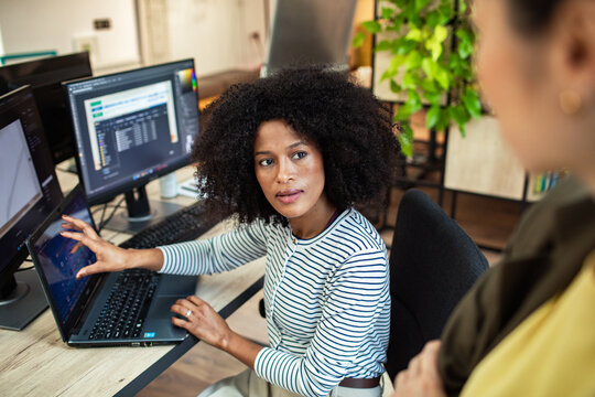 Woman pointing at laptop while discussing with coworker in office