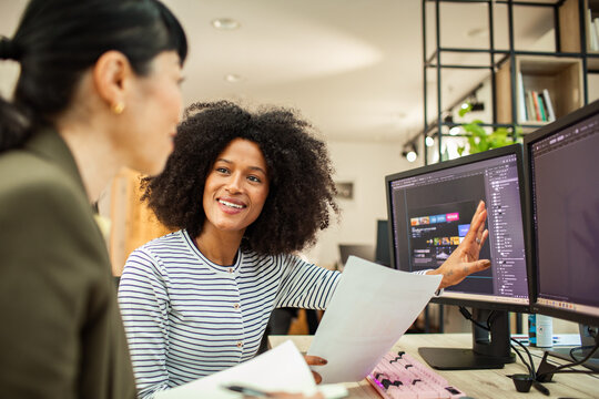 Designer presents web layout to coworker on dual monitors