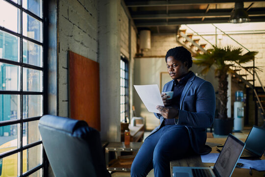Business professional reviewing document while drinking coffee in loft office