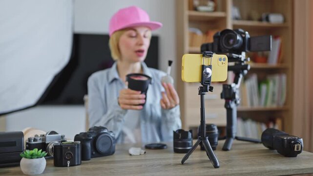 A caucasian woman in a pink cap is filming a tutorial video about photography equipment for her online channel