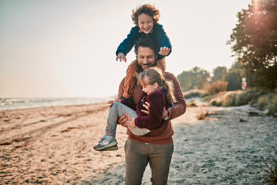 Man carries girl and gives boy a shoulder ride on beach