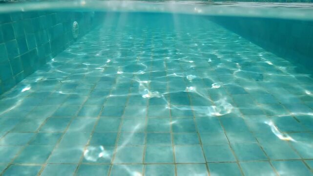 Clear swimming pool water with sunlight caustics dancing over blue tiled bottom in calm motion.