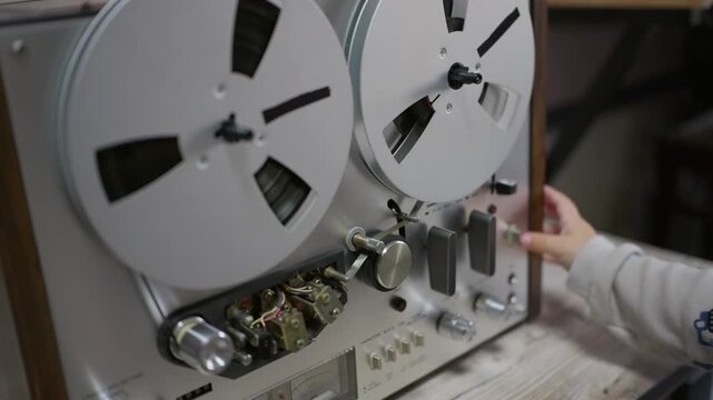 A curious child operates a vintage reel-to-reel audio tape recorder indoors. The tactile cutaway offers rich historical atmosphere, serving sound design stories and documentary edits.