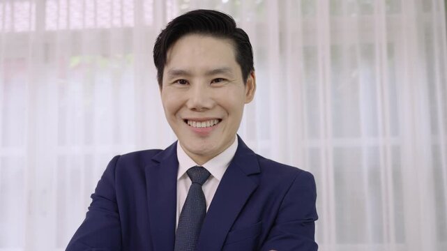Portrait of happy Asian businessman wearing a blue suit is standing smiling with arms crossed while looking at camera in the office. Confident male businessperson with success in corporate business. 