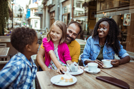 Girl reaches for cupcake as family enjoys coffee at outdoor cafe