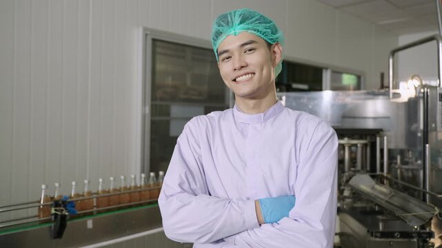 Happy Asian man technician inspector wearing glasses in a uniform of factory relaxing standing smiling with arms crossed while looking at the camera on a production line in the manufacturing industry.