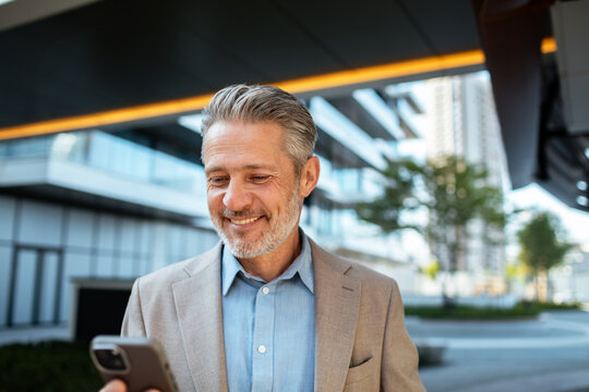 Smiling businessman checking smartphone outside modern office