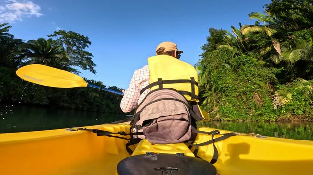 A solo kayak paddling down a large river, surrounded by jungle rainforest scenery in Belize, Central America