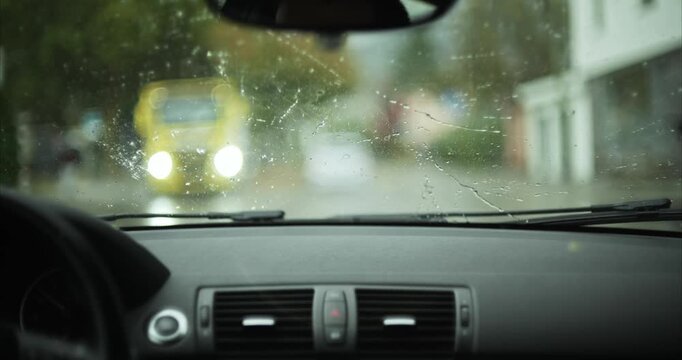 Raindrops on car windshield with oncoming vehicle headlights creating bokeh blur in background on rainy day