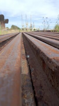 Low Angle Cinematic View Along Rows of Rusty Steel Rails Stacked in Industrial Yard with Port Cranes in Background