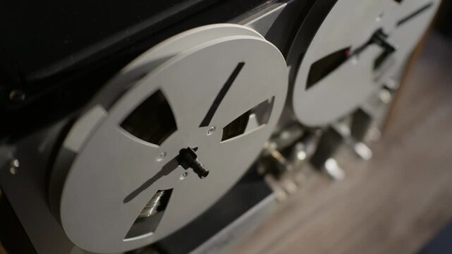 Vintage reel-to-reel audio recorder spins magnetic tape reels in an analog sound studio. The continuous mechanical rotation creates dynamic movement for music productions and podcasts.