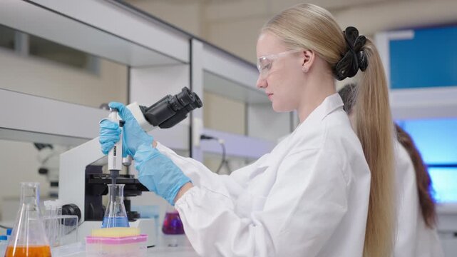 Female scientist and woman researcher technician conducting cosmetic medical laboratory experiment with pipette and microscope, advancing innovation through careful scientific analysis and blue glove