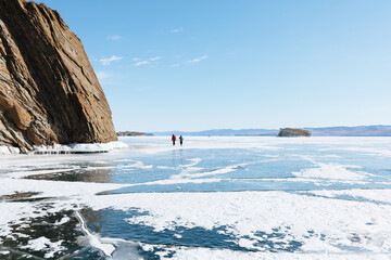 Travelers explore the vast icy surface of frozen Lake Baikal near rocky shores in Irkutsk Oblast, Russia under a clear blue winter sky during seasonal arctic journey © TravelFlow