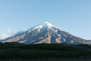 Scenic landscape of snow covered volcanic peak in Kamchatka Krai Russia under clear blue morning sky with volcanic slopes and green wild tundra valley below © TravelFlow
