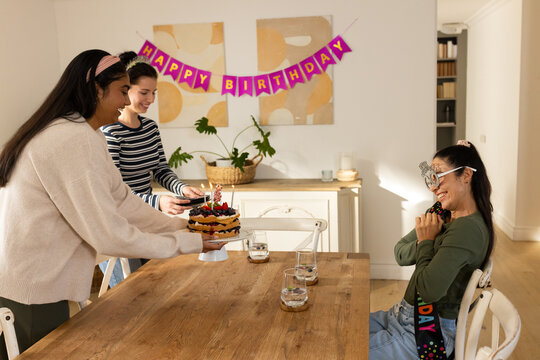 Diverse female friends celebrating at dining table, bringing fruit cake glasses and sash