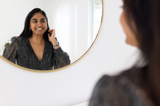 Indian woman adjusting hair in round gold mirror at home vanity with plant, bracelet, earrings