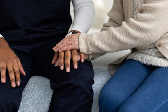 Senior Asian woman placing hand on African American man's hands, navy scrubs, cardigan in room