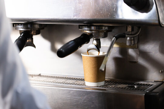 Asian female barista operating espresso machine, pulling shot into brown paper cup