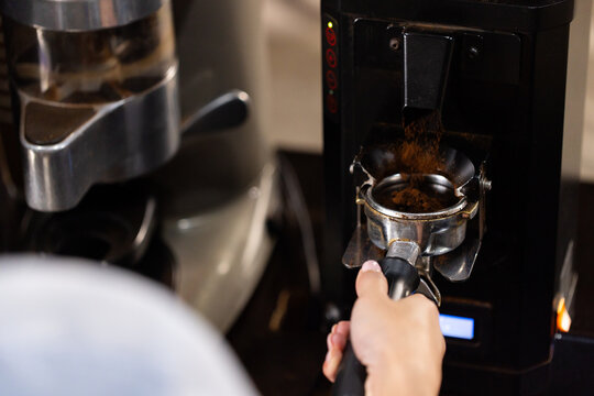 Asian woman holding portafilter catching coffee grounds from grinder at coffee bar, copy space