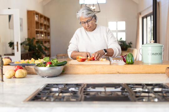 Senior African American female chopping tomatoes on board at wooden island near compost bin