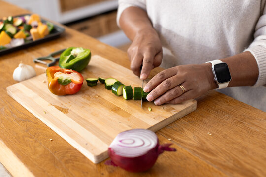 Mature African American woman slicing zucchini into rounds in kitchen on wood board with chef knife