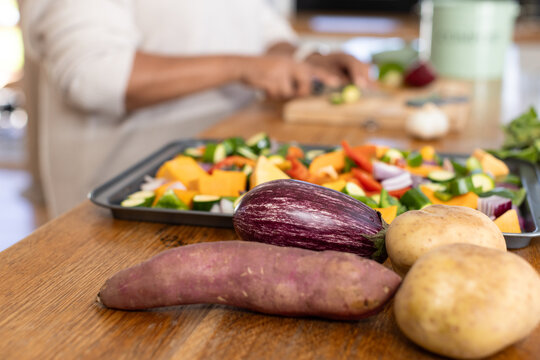 Mature African American woman chopping veg on kitchen counter, root veg eggplant near metal tray