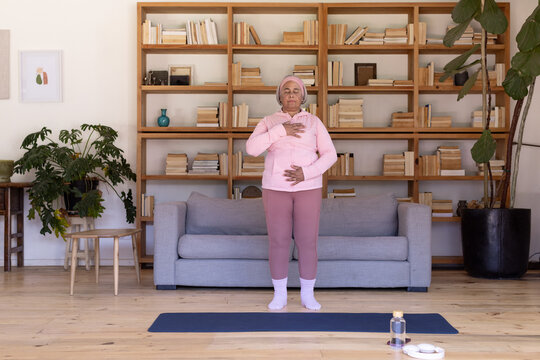 Senior African woman practicing breathing at home on blue mat with water bottle, wearing pink gear