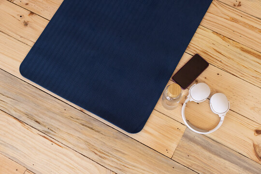 Navy blue yoga mat is resting on light wooden plank floor, with smartphone, water bottle