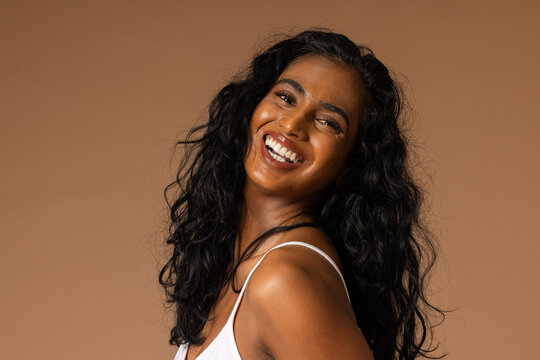 Adult Indian woman smiling and turning over left shoulder in studio wearing white thin-strap top