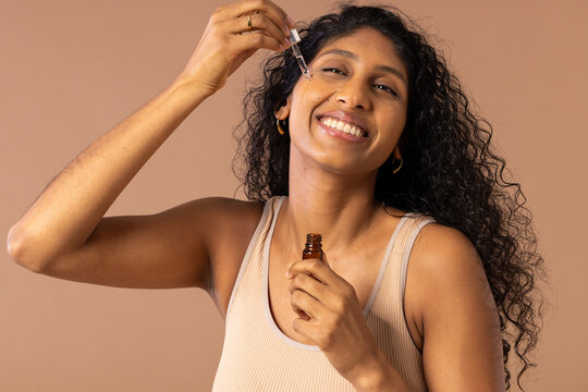 African American woman applying serum with amber dropper bottle, wearing ribbed tank top in studio
