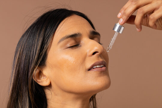 Indian woman tilting back while hand holding dropper with metal cap, serum hovering in studio