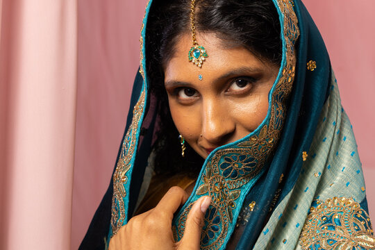 Asian woman wearing embroidered teal shawl, holding edge near chin, showing maang tikka, bindi